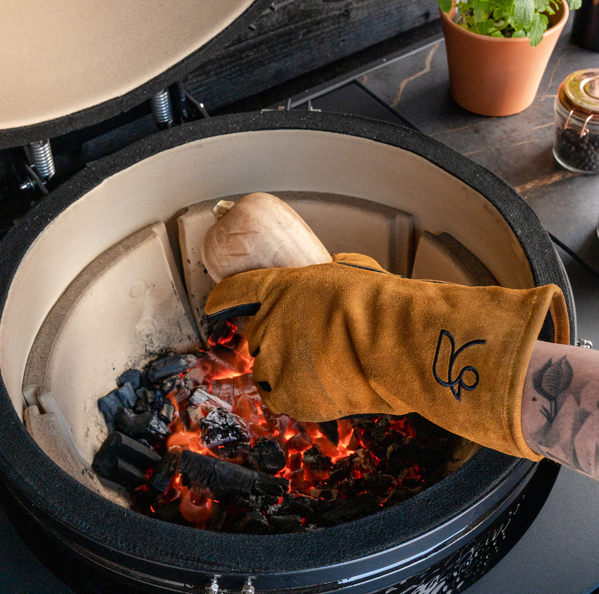Roostr Buitenkeuken barbecue handschoen leer bruin met bbq op de achtergrond